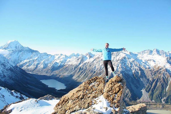 a student standing on the tip of a mountain with more snowy mountains in the background