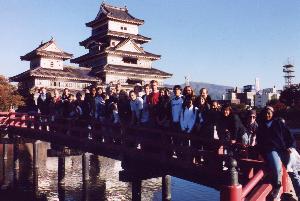 A group photo of students standing on a bridge in front of a pagoda (five story building)